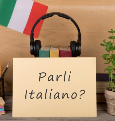Learning languages concept - paper with text "parli italiano?", flag of the Italia, books, headphones, pencils on wooden background