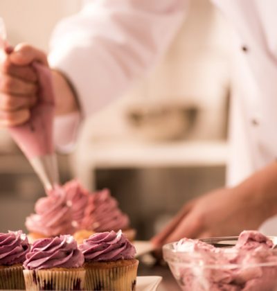 cropped shot of confectioner putting cream on cupcakes