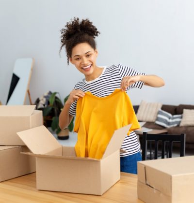 African American female blogger vlogger freelancer using webcam for broadcasting live for his followers, makes an review of ordered clothes, products, goods. Young woman unpacking boxes on camera, smiles friendly