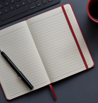 Top view of dark modern workplace with open notebook and red coffee cup on dark grey background