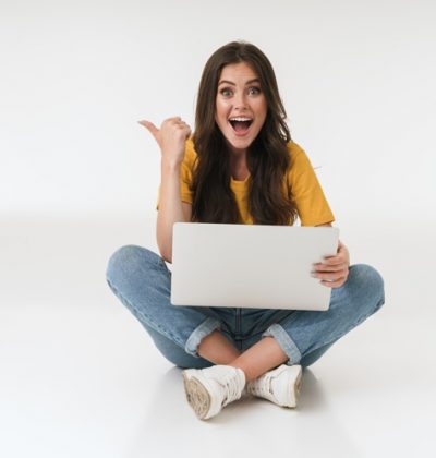 Photo of a emotional surprised cheery young woman isolated over white wall background using laptop computer pointing.